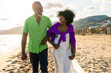 A smiling couple walks arm in arm on a sandy beach during sunset