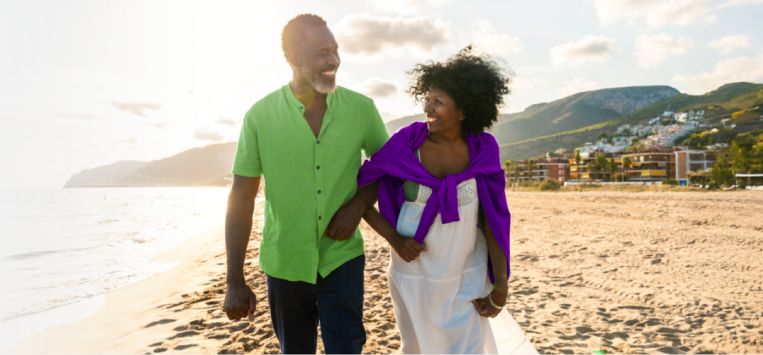 A smiling couple walks arm in arm on a sandy beach during sunset