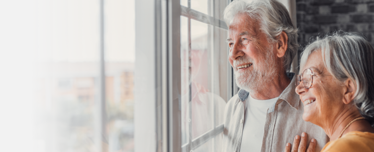 A happy senior couple stands near a window