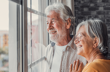 A happy senior couple stands near a window